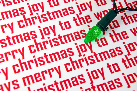 close up of glowing green Christmas light bulb on red and white holiday paperの写真素材