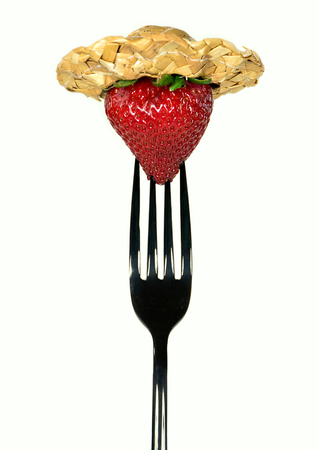 ripe strawberry with straw hat on black fork isolated on white backgroundの写真素材