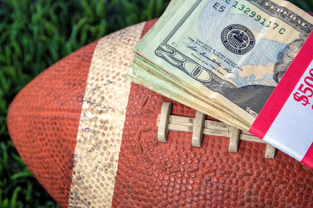 close up of wrapped money stack on used football with green grass backgroundの写真素材