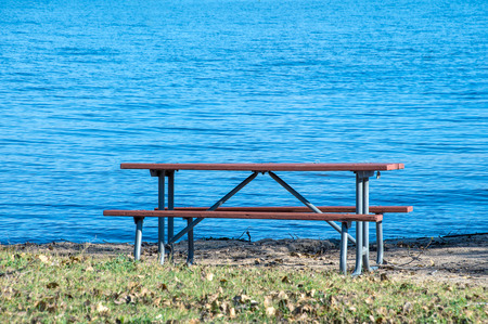 vacant picnic table in sand and grass by blue lake water