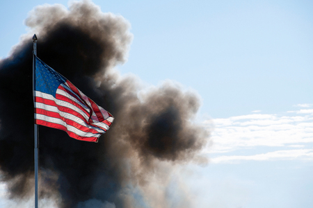 American flag illuminated by sunlight with cloud of black smokeの写真素材