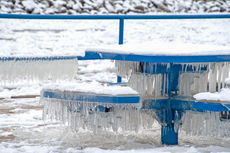 snow and icicles on bright blue park bench and table in Holland Michiganの写真素材