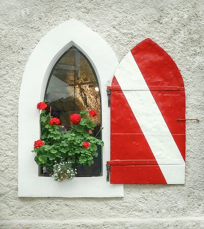 Red geranium plant in European style arch window with red and white striped door and back lit crucifixの写真素材