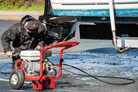 man cleaning underneath boat with pressure washer equipment