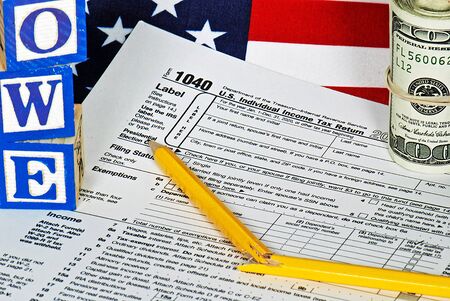 broken pencil and wooden toy blocks on 1040 tax form with money roll and American flag
