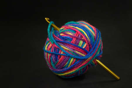 close up of gold crochet hook in colorful variegated yarn ball isolated on blackの写真素材