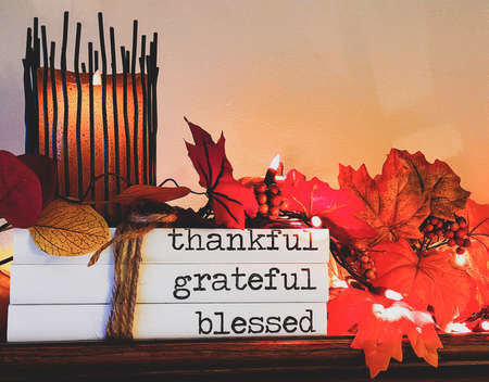 Glowing candle on a stack of Thanksgiving books tied with string and autumn leaves