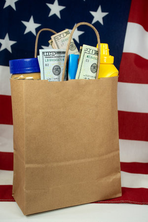 A plain brown paper bag filled with groceries and money on an American flag