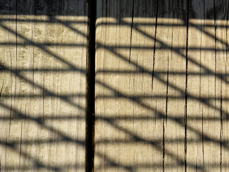 Close-up of lattice fence shadow pattern on brown weathered woodの写真素材
