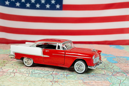 Red and white 1955 Chevy car on a road map with an American flag backgroundの写真素材