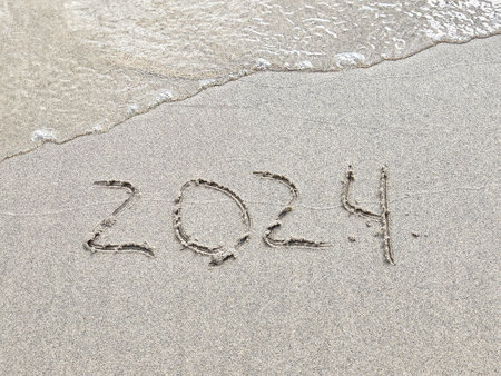 New Year 2024 text in wet beach sand with water bubbles