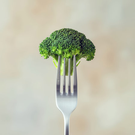A vibrant piece of fresh broccoli pierced on the prongs of a fork, set against a softly blurred backgroundの素材