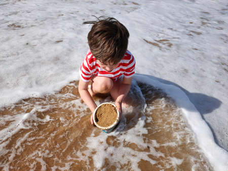 Happy child on the beach in the spring, plays with bucket and sandの写真素材