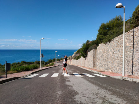 a woman crosses the road along a pedestrian crossing with children in her arms, next to the seaの写真素材
