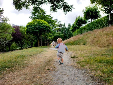 curly-haired child walks in the park with a briefcase behind his backの写真素材