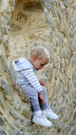 a child sits in the window of a stone house and asks for helpの写真素材