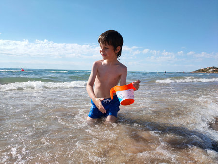 happy child playing in sea waves with watering canの写真素材