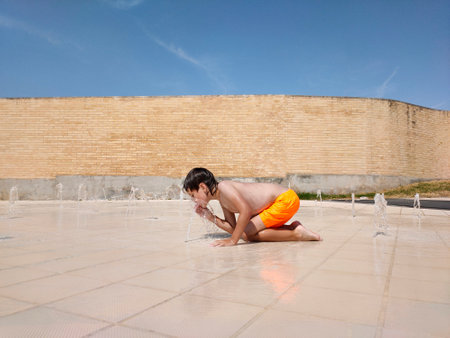 child in the pool drinking water from the fountainの写真素材