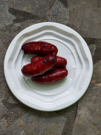 baked sausages on fire lie in a plastic plate on a stone backgroundの写真素材