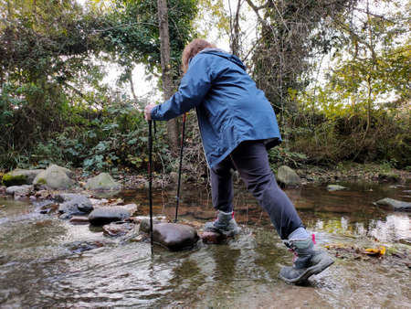 A man in boots who crosses the river on stones, leaning on a caneの写真素材