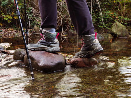legs of a man in boots, crossing the river over the stones, leaning on a caneの写真素材