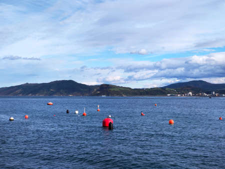 background picture. ocean with red buoys, mountains in the background and blue skyの写真素材