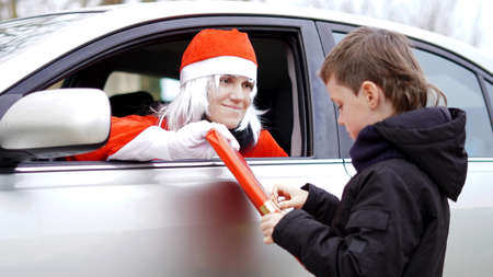 girl dressed as santa claus holding out a gift to the child while sitting in the carの写真素材