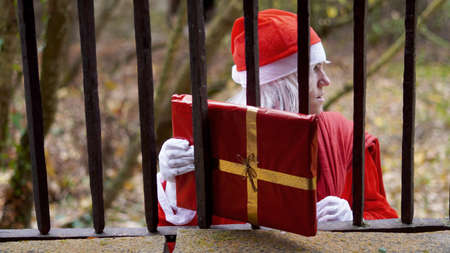 Santa Claus holds out a gift through a barred windowの写真素材