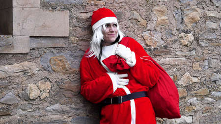 girl dressed as Santa Claus with a bag of gifts on a wall backgroundの写真素材