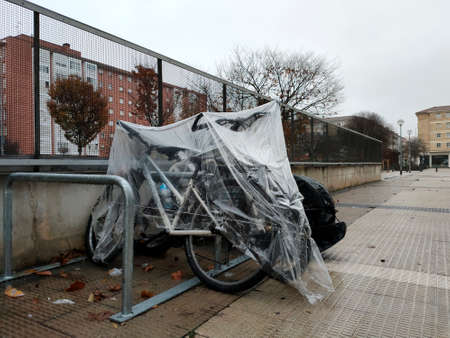 bicycles covered with oilcloth stand on the street. rain December 3, 2021 spain city of pamplonaのeditorial素材