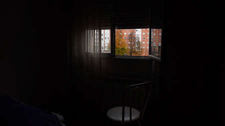 a chair stands by an open window in a dark room