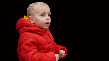 blond child, in a red jacket on a black background, expresses his emotionsの写真素材