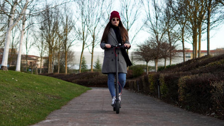 a girl rides an electric scooter in the park, in autumn clothes