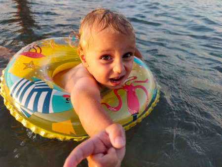 An unhappy child in the sea with an inflatable ring.