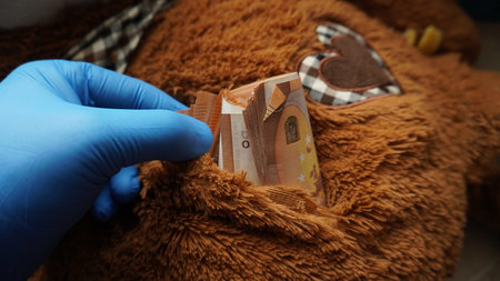 a gloved hand retrieves money from a cache found in a soft toyの写真素材