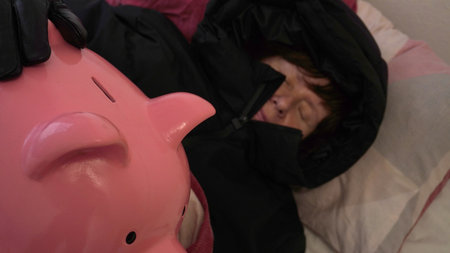 sleeps in a jacket with a hood in an embrace with a piggy bank under the coversの写真素材