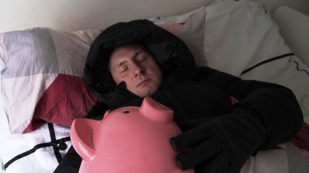 sleeps in a jacket with a hood in an embrace with a piggy bank under the coversの写真素材