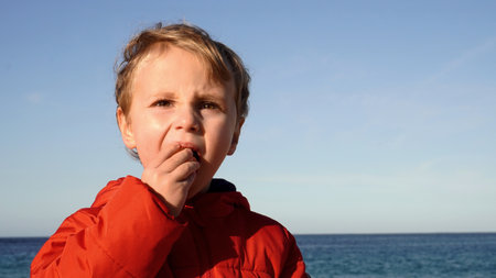 a blonde boy eats mandarin against the backdrop of the sea. close upの写真素材