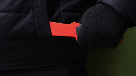 a hand in a black glove pulls a red knife out of the pocket of a black jacketの写真素材