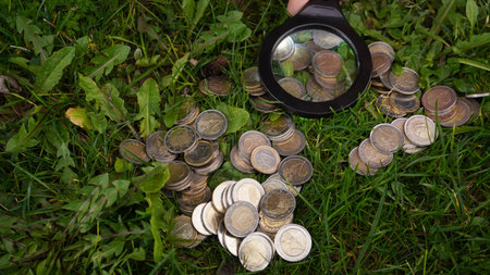 a child plays euro coins on the grass, looking at them through the preclusive glass