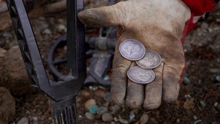 antique silver coins, on the gloved hand, on the background of a metal detector and a shovelの写真素材