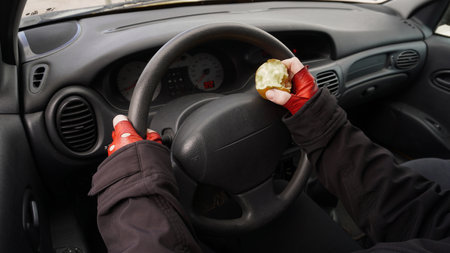 hands on the wheel of a car in red gloves, with an apple in one hand a person drives a car. Concept: Eating while driving a carの写真素材