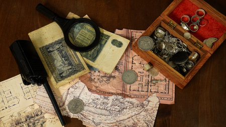 jewelry box, jewelry, silver coins, walkie-talkie, paper money lie next to old blueprints of an abandoned house on a wooden table concept: treasure hunt in abandoned housesの写真素材