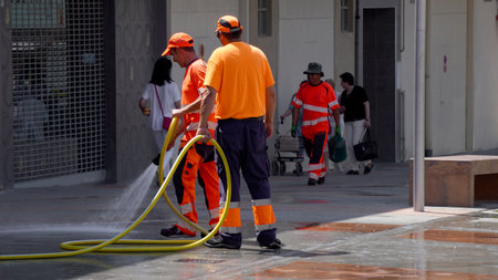 people in bright orange uniforms are pouring water on the streets from a hose. cleaning the streets after the festivities Mutilva (Navarra) June 25, 2023のeditorial素材