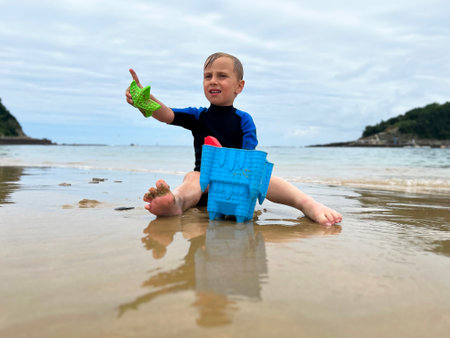 a mischievous boy, on the ocean shore in a neoprene suit, gesturing with his finger in displeasureの写真素材