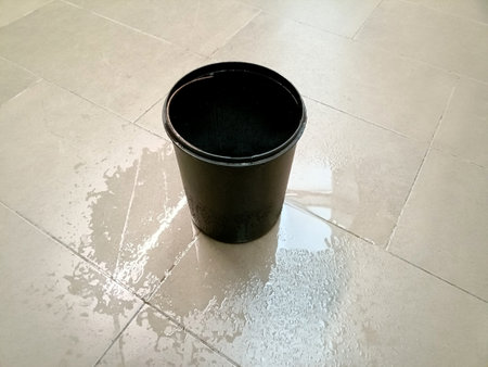There is a bucket on the floor into which water is dripping from the ceiling. concept: roof repair requiredの写真素材