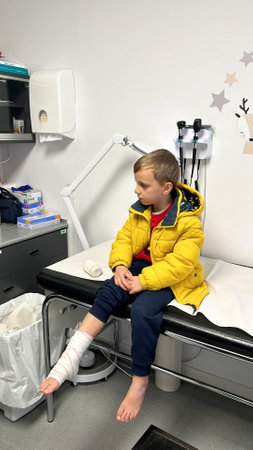 child in winter jacket with bandaged leg sits in emergency room. Concept: caution during winter sportsの写真素材