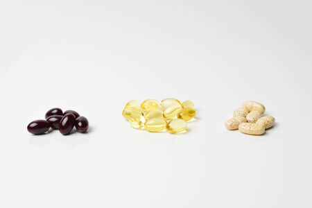 Fish oil, multivitamins  and astaxanthin capsules in three bunches. Omega-3 in the middle. White background. Close-up.の写真素材