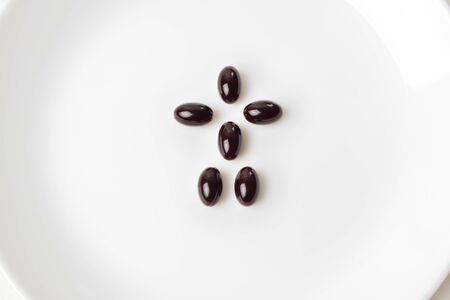 Astaxanthin pills form a human shape on the white plate. Close-up.の写真素材