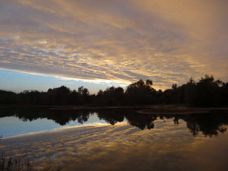 Sunset on the lake with trees and clouds reflected in the waterの写真素材